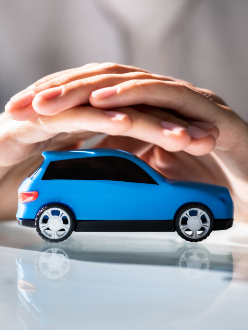 Representação do seguro automotivo. Maquete de um carro azul sobre uma mesa branca espelhada, protegido por duas mãos.